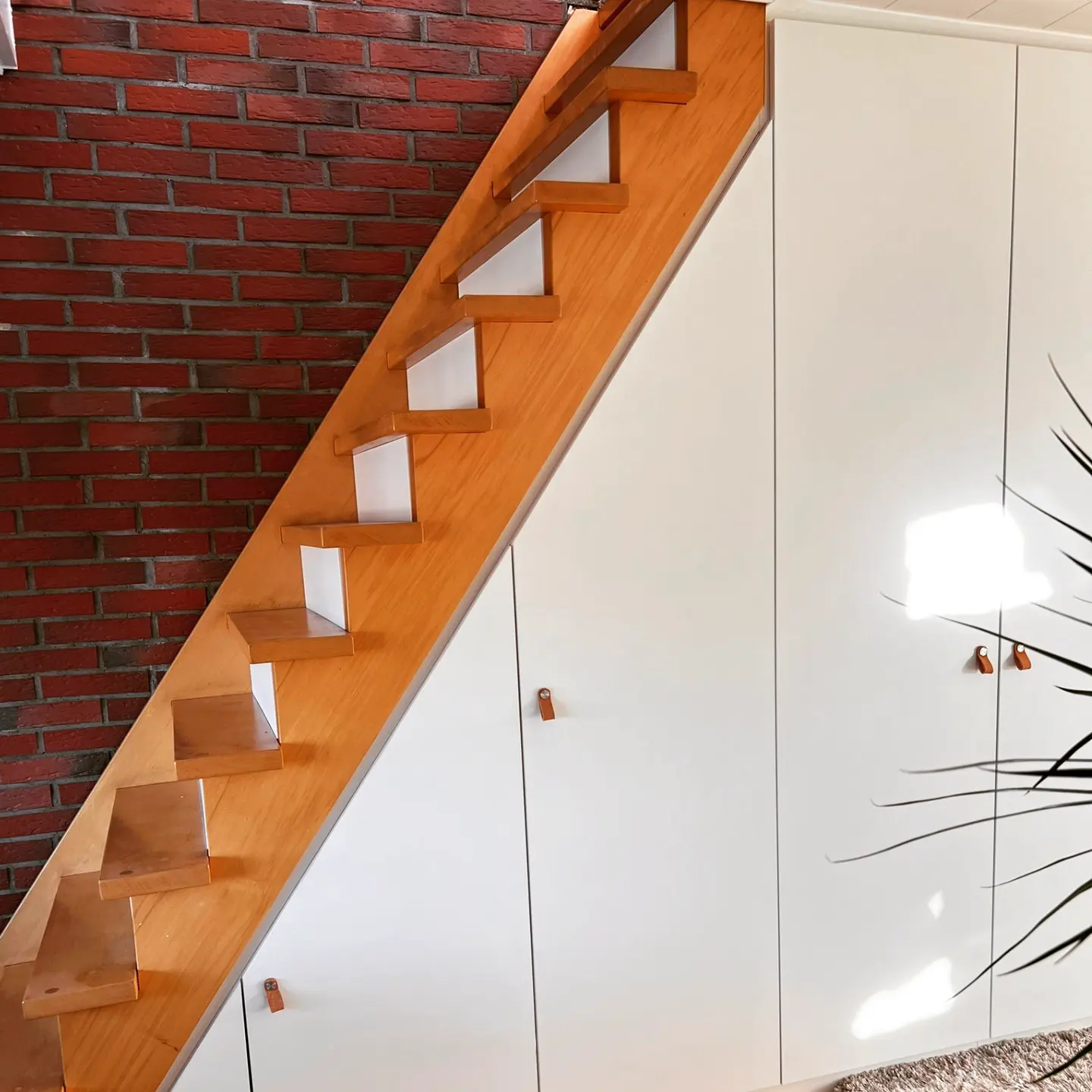 Holztreppe an Klinkerwand mit weißen Einbauschränken darunter